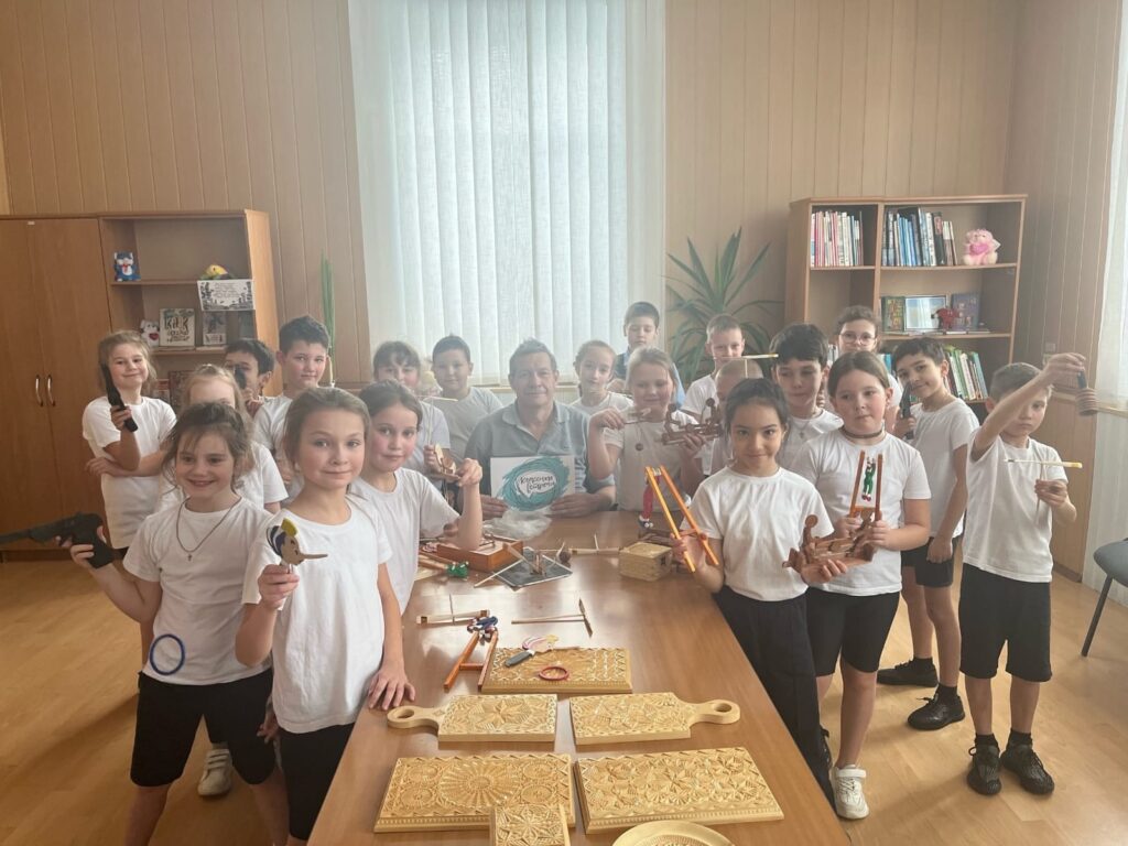 Флуз Рафкатович среди учеников начальных классов после творческого занятия. Дети гордо демонстрируют сделанные игрушки и поделки.