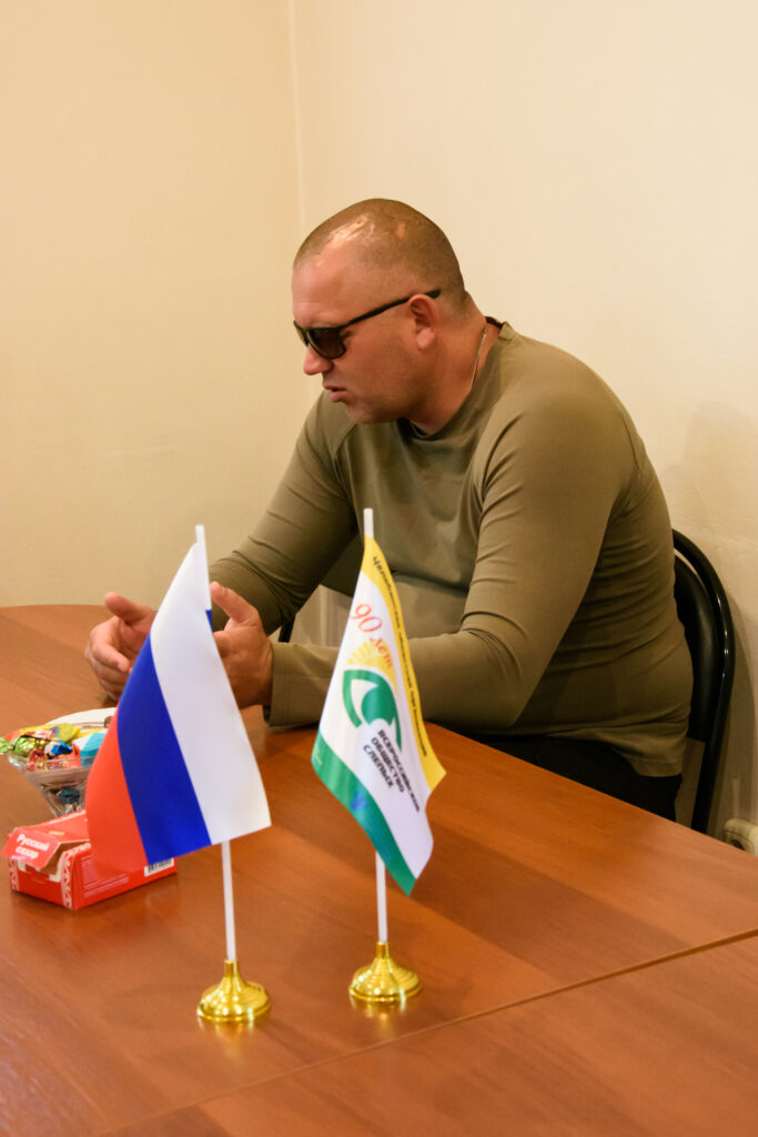 Участник СВО Сергей Трубников на встрече в ЧООО ВОС. На переднем плане — флажки России и Всероссийского общества слепых.