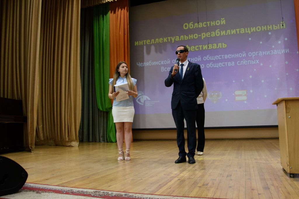 На открытии областного интеллектуально-реабилитационного фестиваля: председатель ЧООО ВОС Александр Рожков обращается с приветственным словом, рядом ведущая мероприятия.