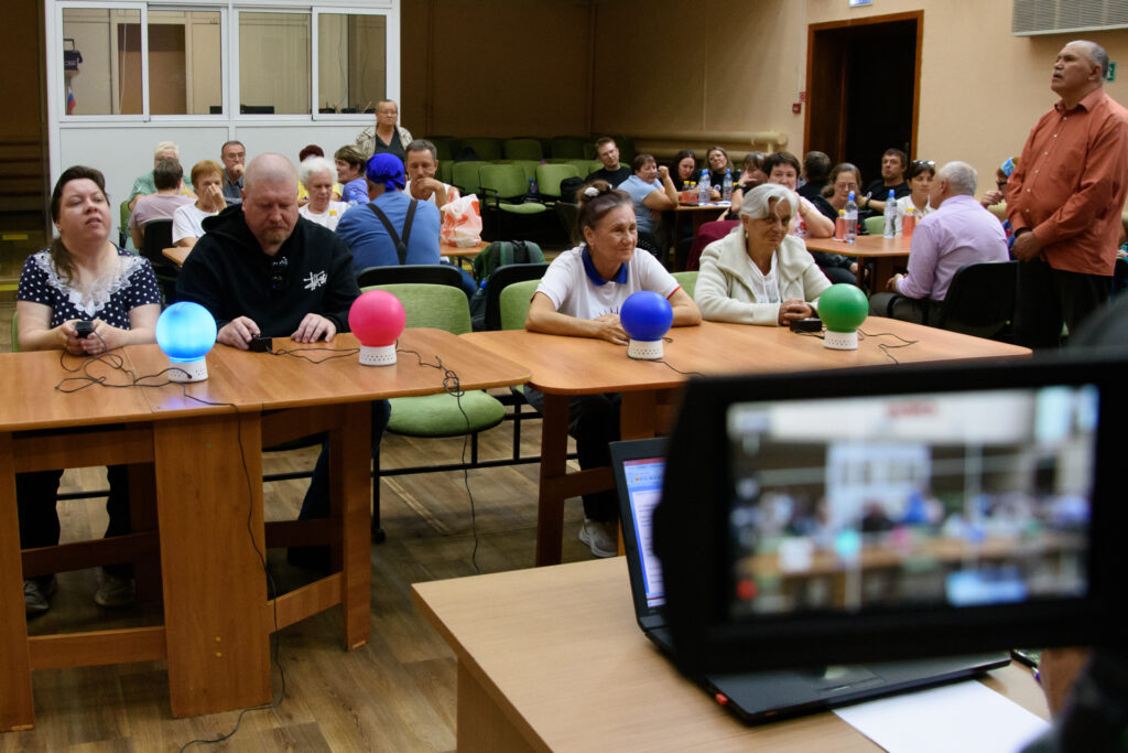 Участники фестиваля отвечают на вопросы в блиц-турнире «Ответь за 1 минуту». Перед ними установлены специальные устройства со световыми сигналами, фиксирующими скорость ответа. Атмосфера напряжённая и азартная.