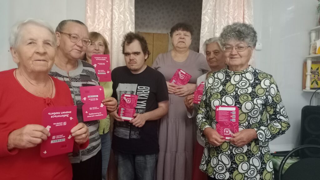 группа участников праздника с подарками в руках. Все держат яркие розовые наборы, улыбаясь в камеру.