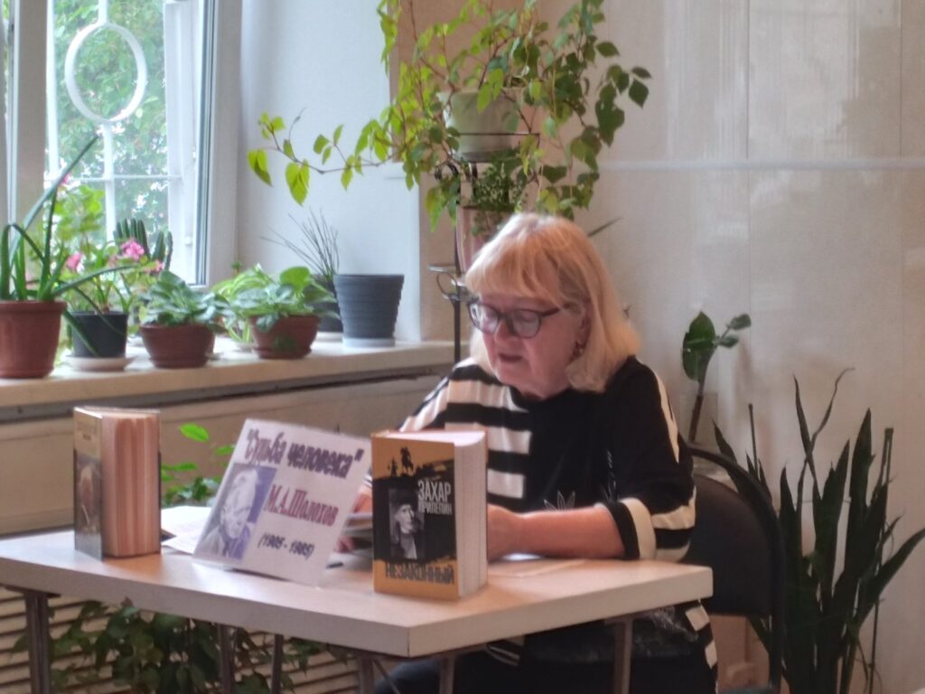 Женщина в очках читает текст за столом. На столе книги и табличка с портретом Михаила Шолохова и надписью: «Судьба человека».
Фото 3. Мужчина и две женщины стоят у стола с книгами и табличкой о Шолохове. Перед ними сидят участники мероприятия, большинство в тёмных очках. На стене — плакат Чебаркульской МО ВОС.
Если нужно, могу адаптировать текст ещё точнее под стандарты доступности.
Спросить ChatGPT