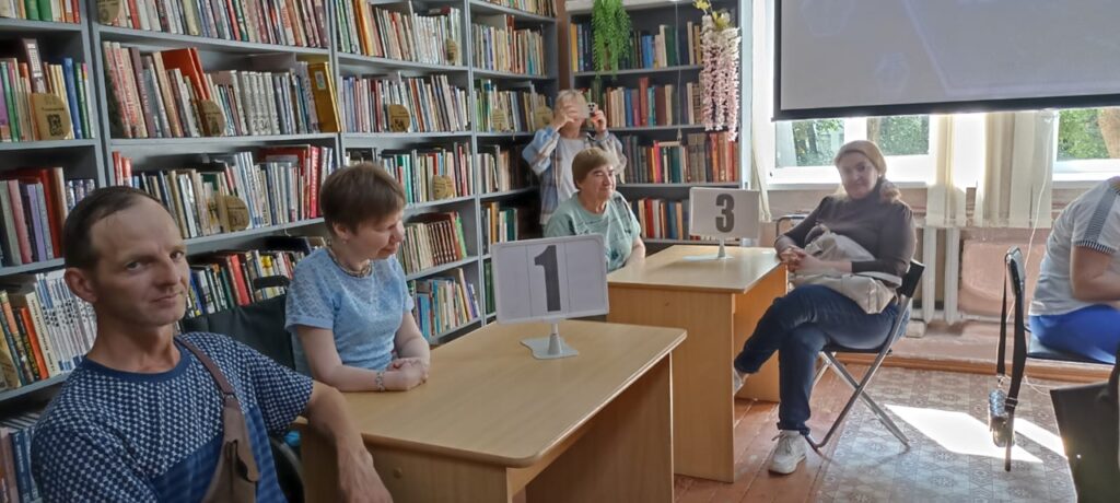 Участники интеллектуальной игры сидят за столами с табличками командных номеров в читальном зале библиотеки
