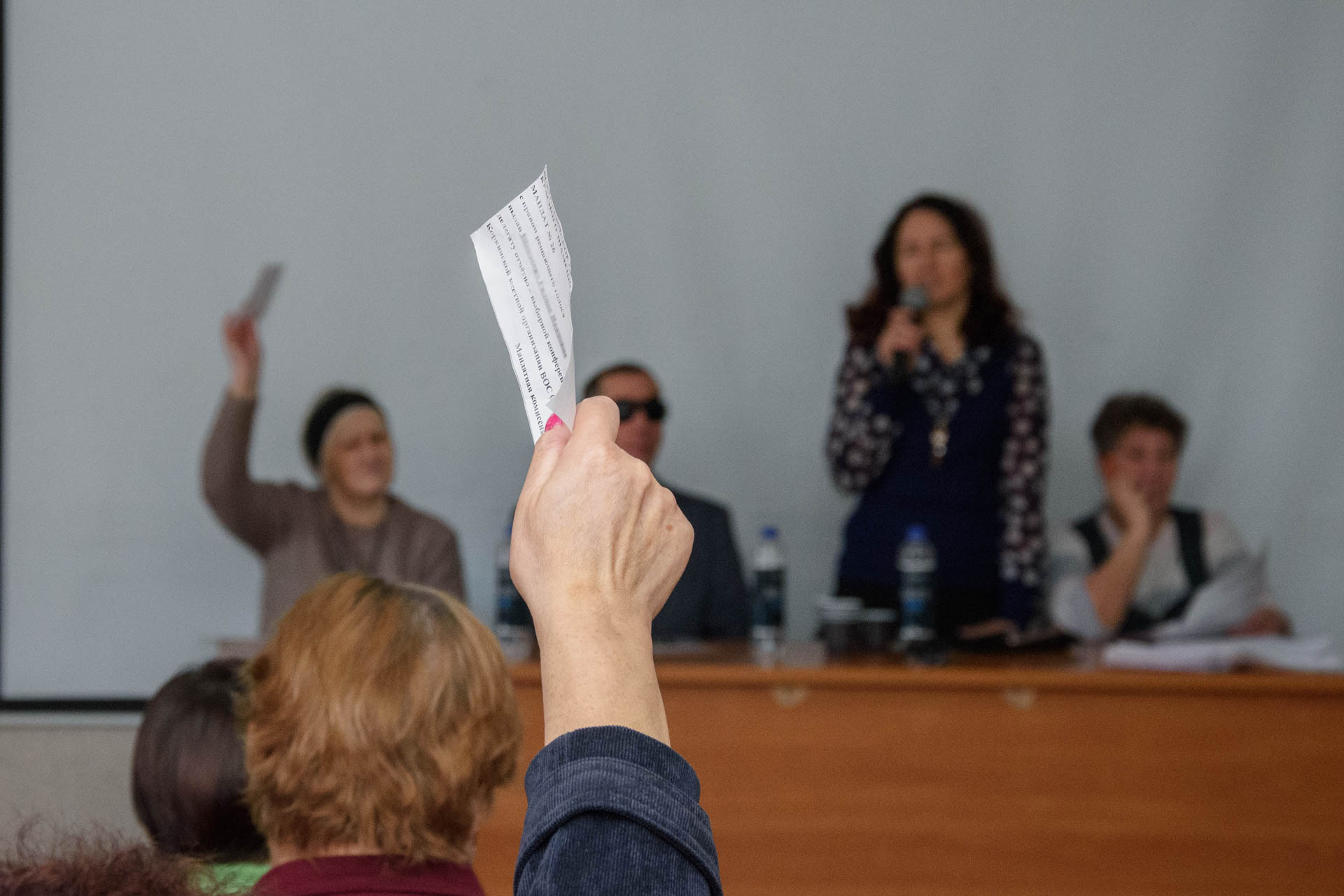 на фоне выступления и.о. председателя коркинской мо вос на переднем плане рука с поднятым мандатом