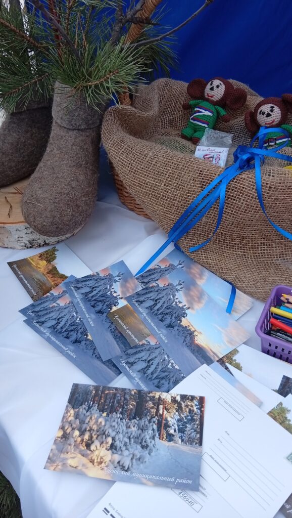 открытки с зимними пейзажами, валенок с еловыми ветками, корзина с вязаным Чебурашкой и цветные карандаши.