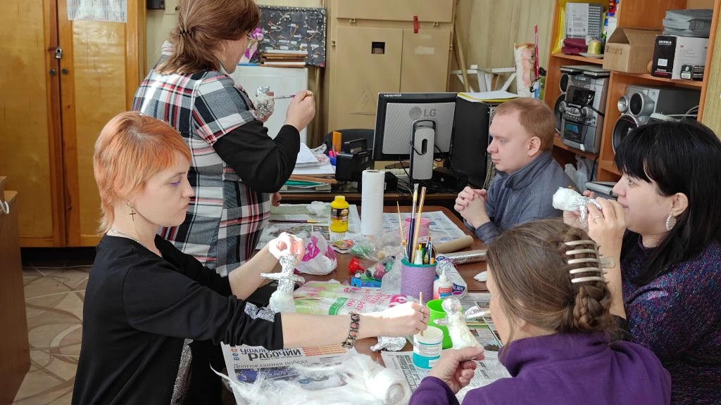 Несколько участников клуба за столом занимаются рукоделием: делают фигурки из фольги, на столе клей, кисточки и другие материалы.