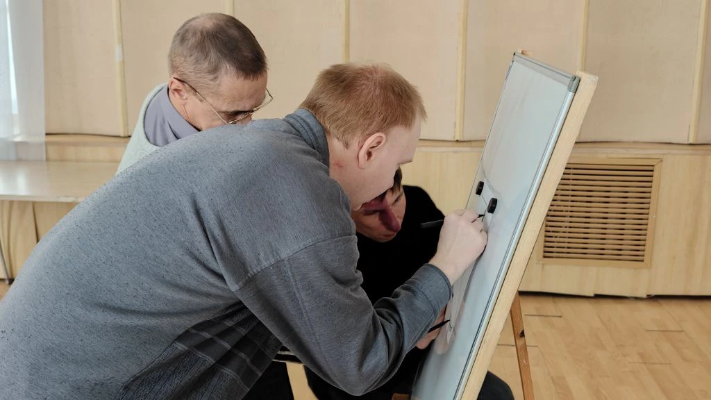 Двое мужчин у магнитной доски; один пишет маркером.