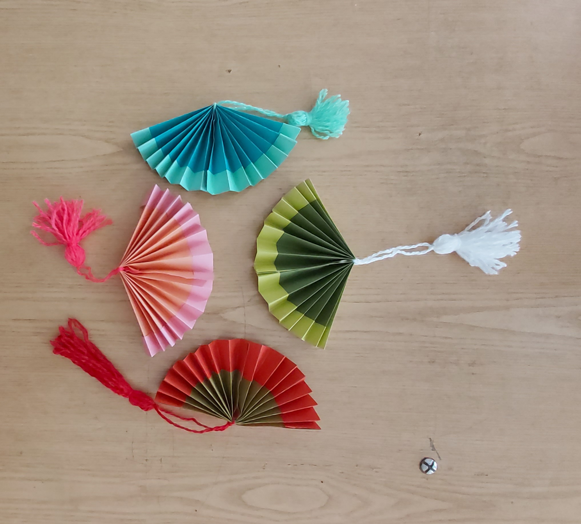 4 бумажных веера с кисточками: бирюзовый, розово-оранжевый, зелёный с салатовой кромкой, красный с тёмно-оливковым. Внизу справа маленький металлический винт.