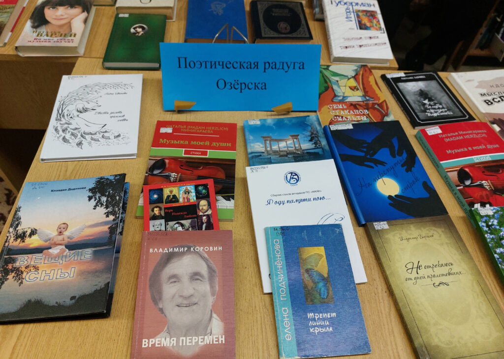 На фото книжная выставка на столе; в центре табличка: «Поэтическая радуга Озёрска». Вокруг разложены книги/сборники, среди читаемых: «Музыка моей души» (Наталья Минигареева), «Вещие сны», «Время перемен» (Владимир Коровин), «Я одну памяти пою…», «Не отрекаюсь от дней пролетевших…».