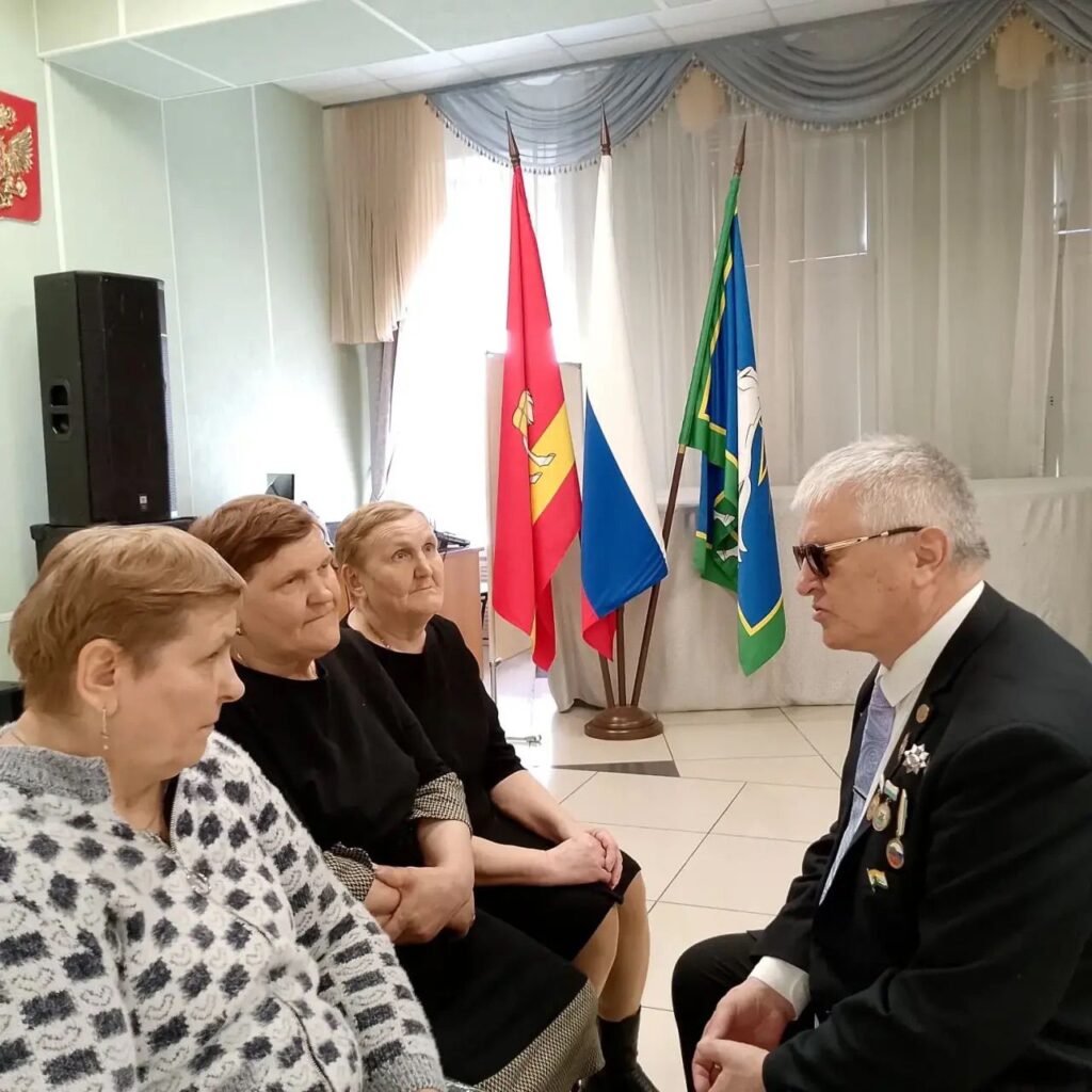 Трое женщин сидят напротив председателя чебаркульской мо вос; они разговаривают, на фоне стоят флаги.