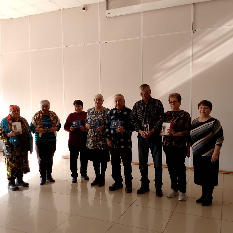 Группа из восьми человек стоит в помещении у светлой стены, некоторые держат в руках книги или папки.