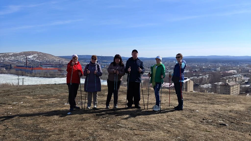 Шесть человек с палками стоят на сухом холме и позируют на фоне панорамы города и далёких гор; слева виден участок снега.