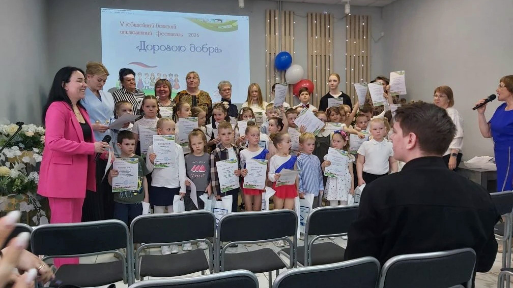 На сцене большая группа детей и взрослых с грамотами, это награждение на фестивале «Дорогою добра» 2026; слева и справа стоят ведущие с микрофонами, в зале перед ними ряды стульев с сидящими зрителями.