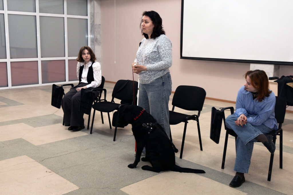 надежда и ронда рассказывают о собаках-проводниках. надежда стоит перед студентами, рядом у ноги сидит ронда