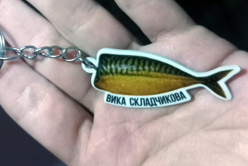 Брелок на цепочке в форме рыбы (жёлто‑зелёная с тёмными полосами).
Текст: ВИКА СКЛАДЧИКОВА