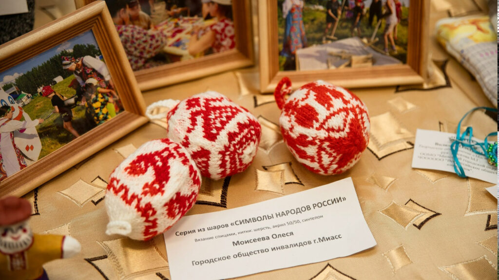 Три вязаных бело‑красных шара с орнаментом.
Подпись: серия «Символы народов России», автор Моисеева Олеся