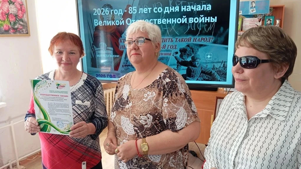 Три женщины стоят у экрана с надписью про 85‑летие начала Великой Отечественной войны; левая держит благодарственное письмо.
