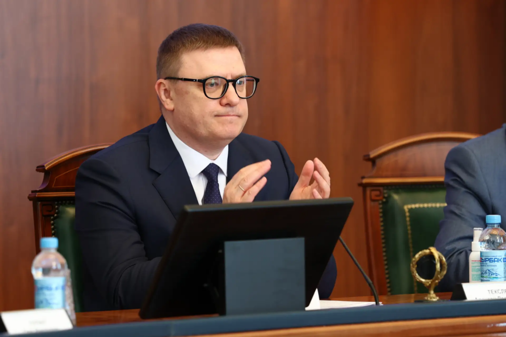 Алексей Текслер в тёмном костюме и очках сидит за столом заседания перед монитором