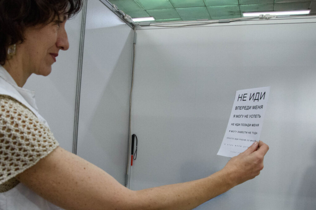Женщина держит перед собой лист с крупным текстом.
На листе написано:
НЕ ИДИ ВПЕРЕДИ МЕНЯ, Я МОГУ НЕ УСПЕТЬ, НЕ ИДИ ПОЗАДИ МЕНЯ
Я МОГУ ЗАВЕСТИ НЕ ТУДА, 
ПРОСТО ИДИ РЯДОМ СО МНОЙ И БУДЬ МОИМ ДРУГОМ