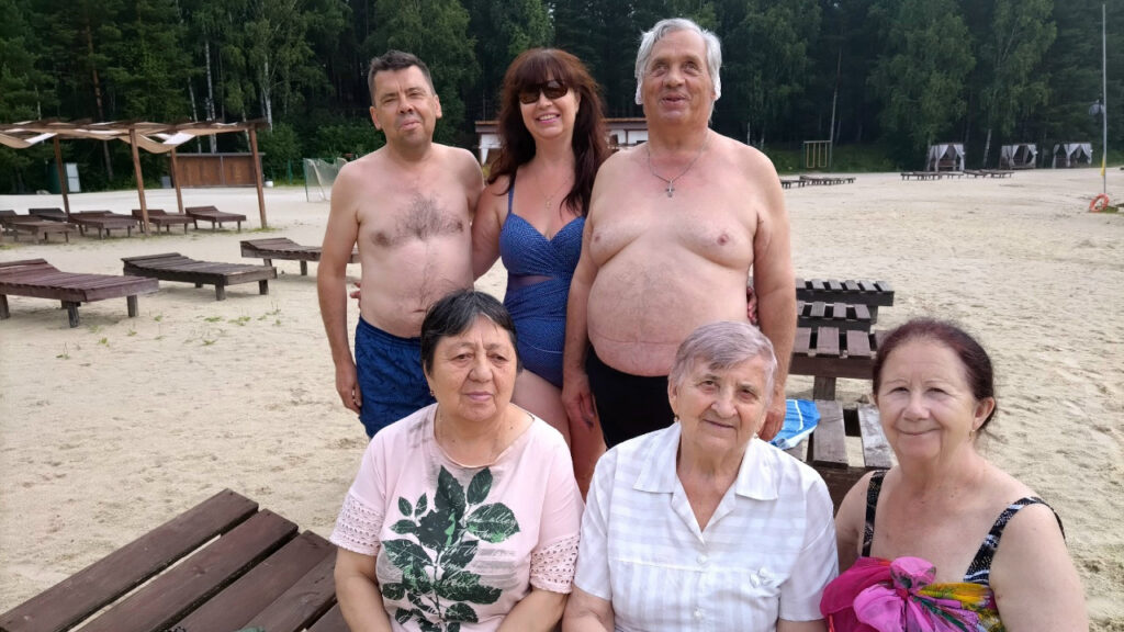 Шесть человек на пляже: сзади двое мужчин и женщина в купальнике, спереди три пожилые женщины сидят на скамейке