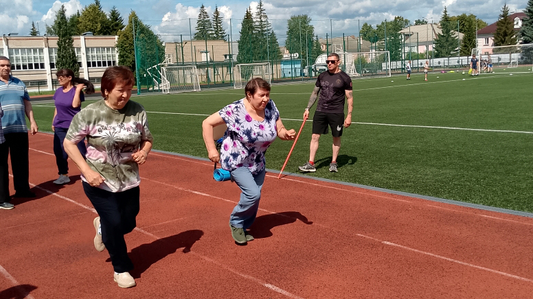 Женщины бегут по беговой дорожке стадиона, сзади стоит мужчина с флажком и наблюдает.