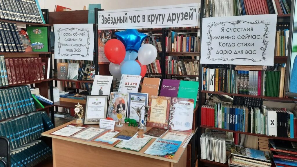 Книжная выставка в библиотеке: на столе дипломы, грамоты, книги и кубки, над ними шары; сверху плакат «Звёздный час в кругу друзей» и две юбилейные надписи про 75‑летие и стихи.