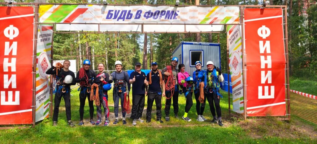 Спортсмены Челябинской области в туристском снаряжении фотографируются у финишной арки после прохождения дистанции.