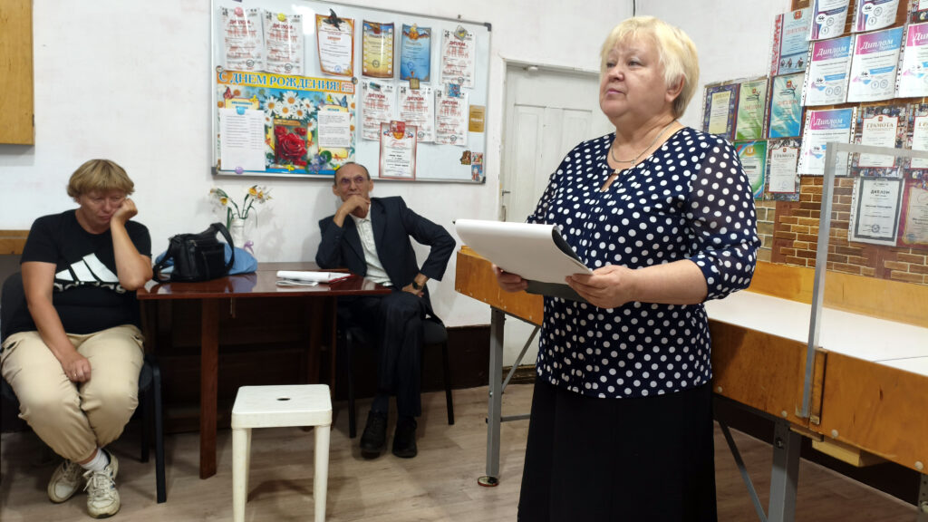 Участница литературной встречи читает произведение по листам перед слушателями.