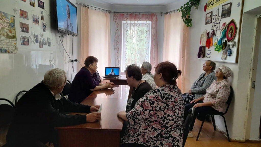 Участники клуба «Забота» смотрят фильм и обсуждают его за общим столом.