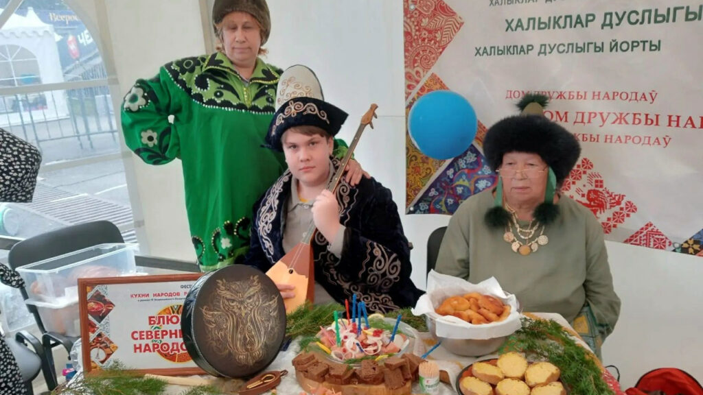 Фото 6. Участники в национальных костюмах позируют у стола с блюдами северных народов и музыкальными инструментами.