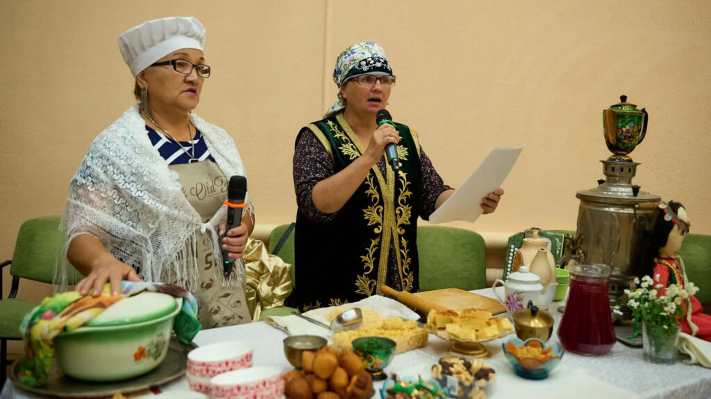 Участницы татаро-башкирской команды представляют национальную кухню; на столе — выпечка, посуда, самовар и другие угощения.