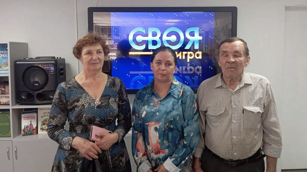 Победители и призёры «Своей игры» фотографируются на фоне экрана с заставкой интеллектуальной викторины.