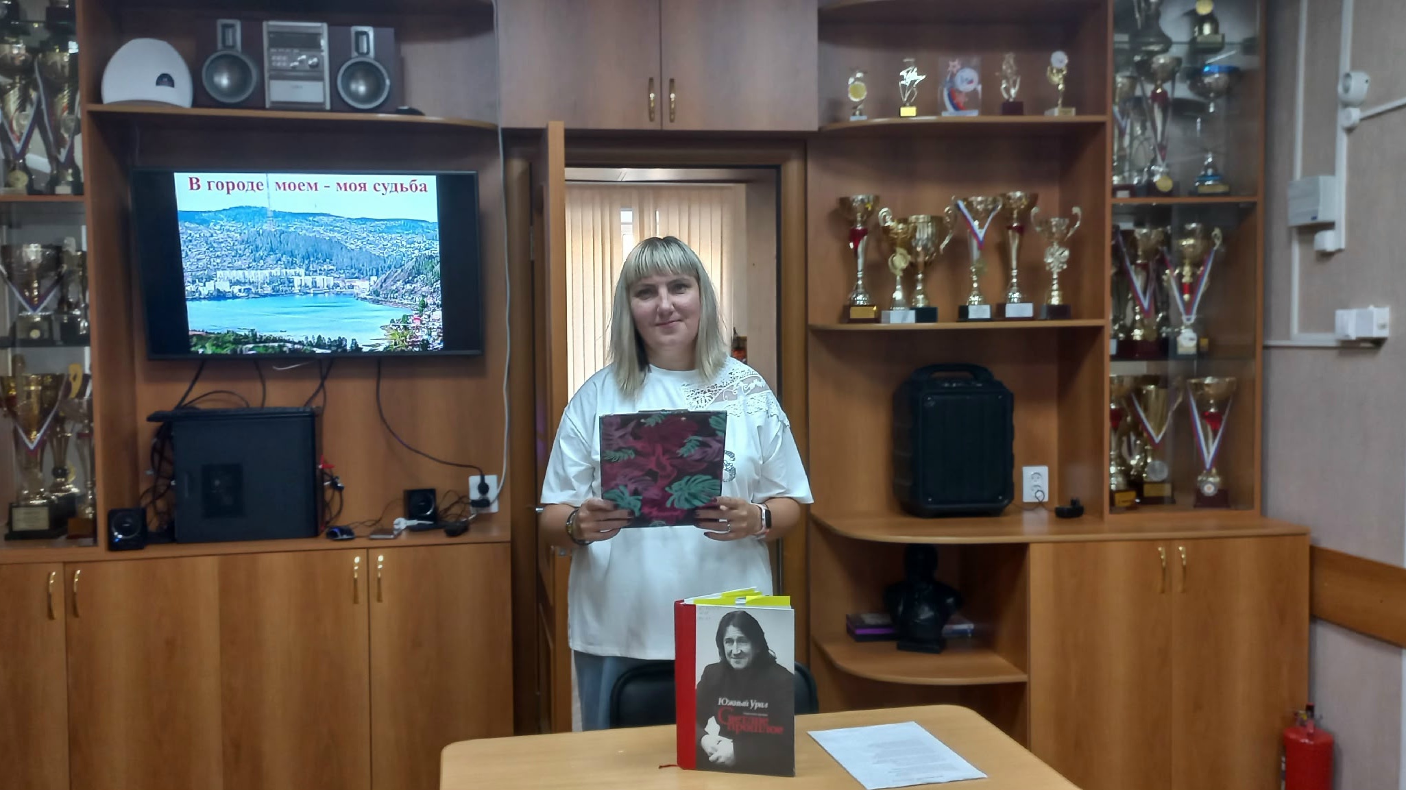 Библиотекарь проводит тематическую встречу о Златоусте; рядом размещены книги, а на экране показана презентация «В городе моём — моя судьба».