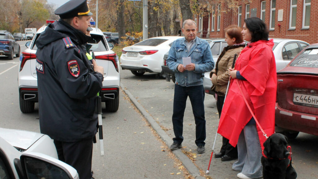 Надежда Завей-Борода, представитель библиотеки и сотрудники Госавтоинспекции беседуют у припаркованных автомобилей.