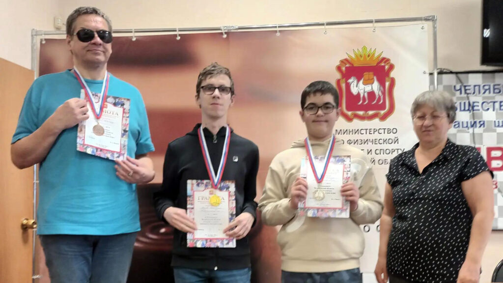 Мужчина и двое юношей с медалями и грамотами за призовые места в чемпионате Челябинской области по шахматам. Справа стоит представительница организаторов соревнований.