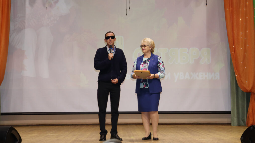 Мужчина выступает с микрофоном рядом с женщиной, держащей награду.