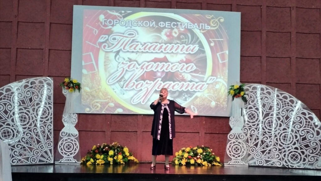 Женщина исполняет песню на сцене городского фестиваля «Таланты золотого возраста».